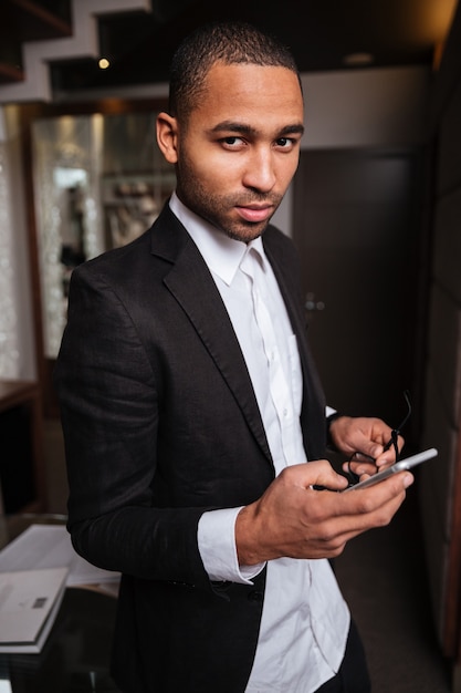 Vertical image of african man in suit standing in hotel with phone and