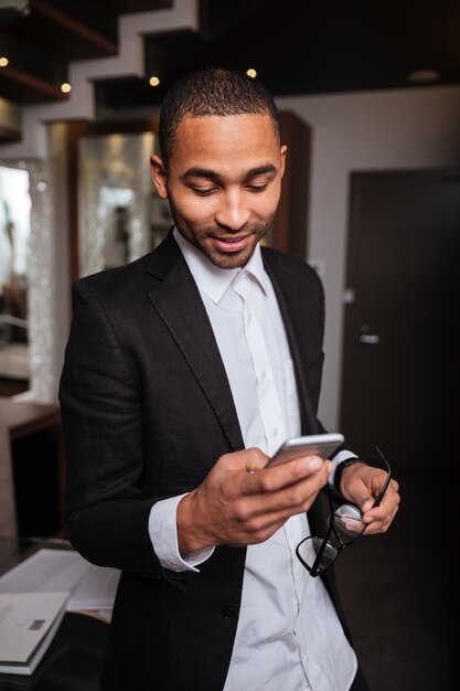 Vertical image of african man in suit using phone in hotel