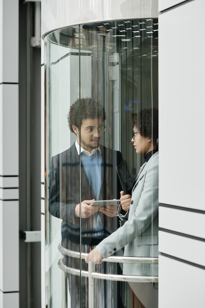 Vertical image of business couple using digital tablet and talking during their meeting in elevator