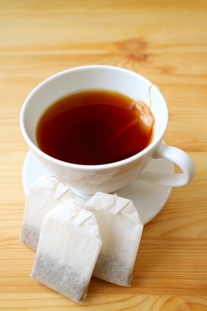 Vertical image of a cup of hot tea with tea bags on a wooden table