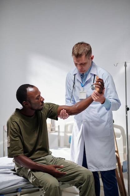 Immagine verticale del medico in camice bianco che esamina il braccio del soldato durante la sua visita in clinica