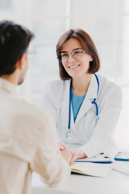 Vertical image of female doctor reassures her male patient, hold hand and talk calmly about illness cure