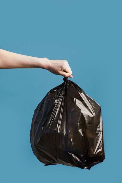 Vertical image of female hand holding black trash bag, waste sorting and recycling concept