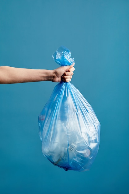 Vertical image of female hand holding trash bag with plastic, waste sorting and recycling concept