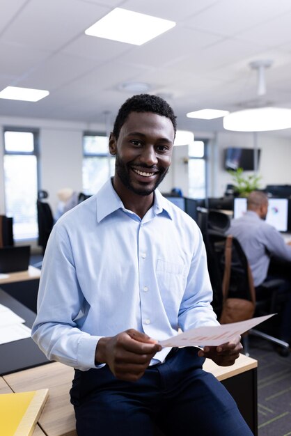Photo vertical image of happy african american businessman looking at camera in office. business professionals, job, corporation and working in office concept.
