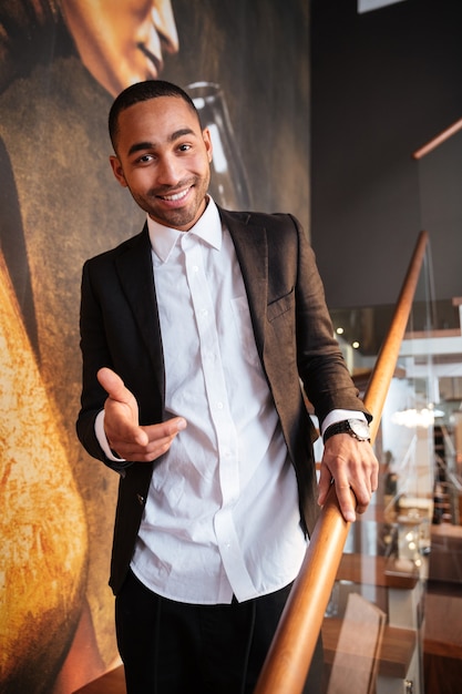 Vertical image of happy african man in suit standing on stairs and pointing