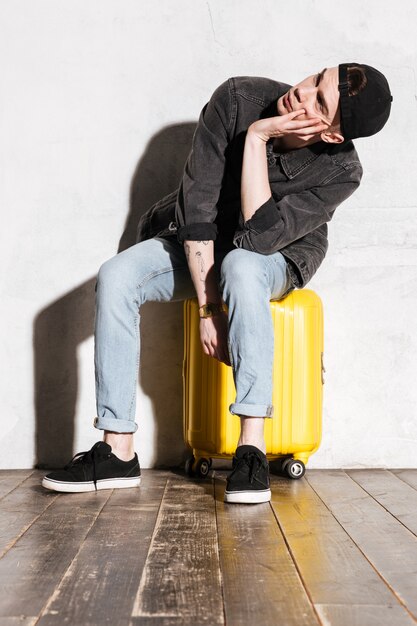 Vertical image of Hipster in snap back waiting on suitcase