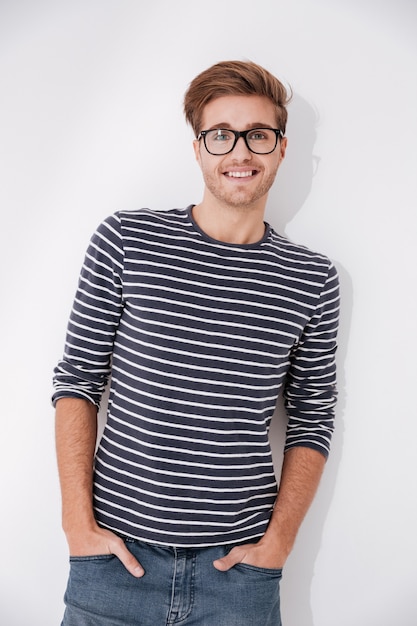 Vertical image of man in striped sweater and glasses posing with arms in pockets and looking at camera. Isolate gray background