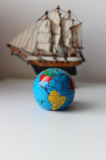 Vertical Image Of Miniature Globe In Front Of Mast Ship Model Isolated On White Backdrop