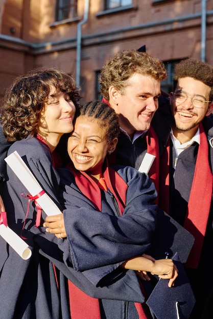 Фото Вертикальное изображение счастливых студентов, обнимающих друг друга, заканчивающих университет