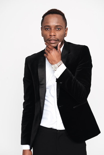 Vertical image of pensive african man in suit looking at camera and holding hand near the face. Isolated white background