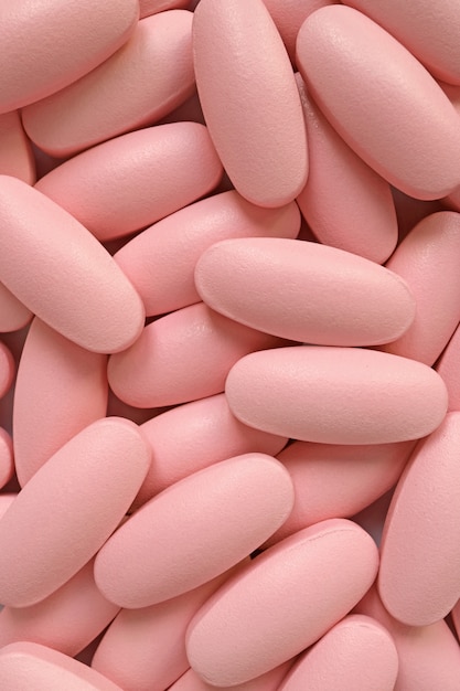 Vertical image of pile of pastel pink oval shaped pills