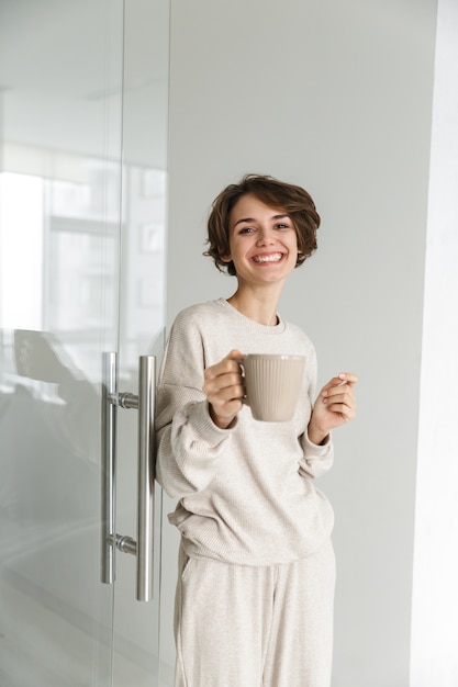 Vertical image of Smiling brunette woman drinkng coffee at home