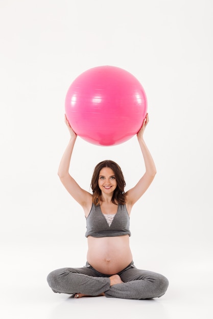 Vertical image of smiling pregnant woman sitting on the floor