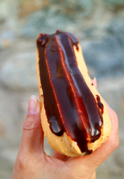 Вертикальное изображение вкусного шоколадного эклера в руке