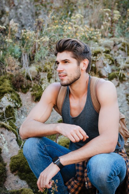 Photo vertical image of traveling man near the rock. sitting squatting