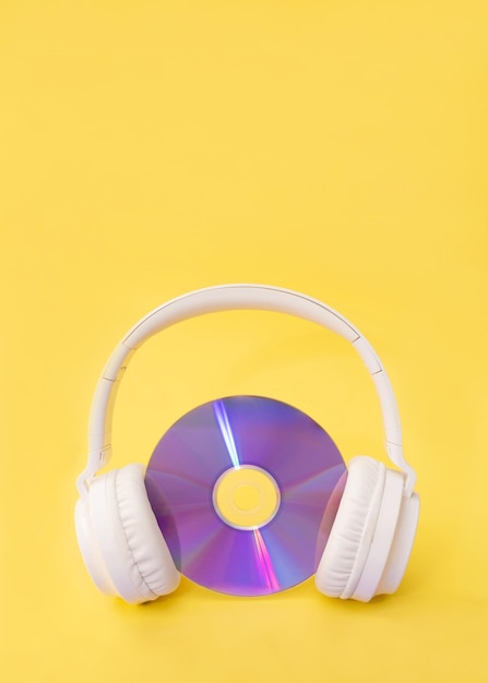 vertical image of white wireless headphones listening a purple compact disc on a yellow background
