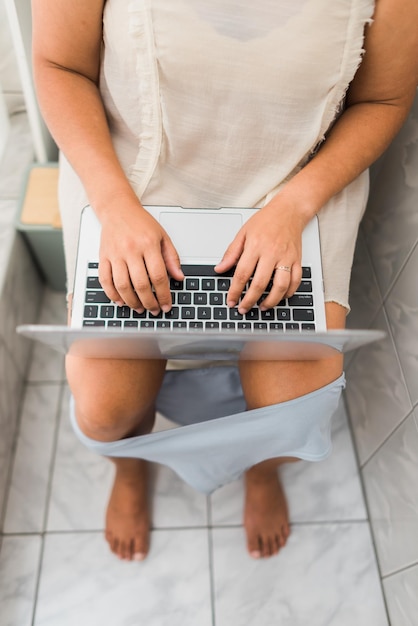 Vertical image of a workaholic woman using her computer in the bathroom