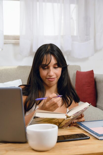 ラテン系の若い黒人女性が自宅で座って勉強しノートに書き留めています