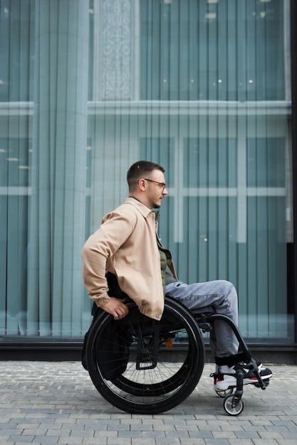 Вертикальное изображение молодого человека с инвалидностью, едущего в инвалидной коляске по городу