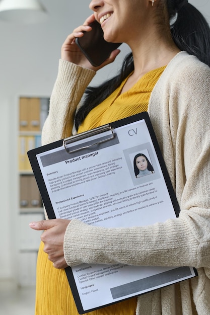 Photo vertical image of young pregnant businesswoman with resume talking to new candidate on mobile phone