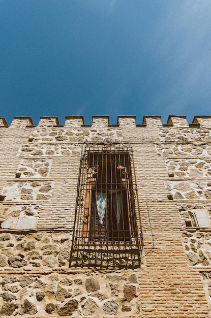 Vertical low angle shot of a stone building in Toledo Spain with metal bars covering its window