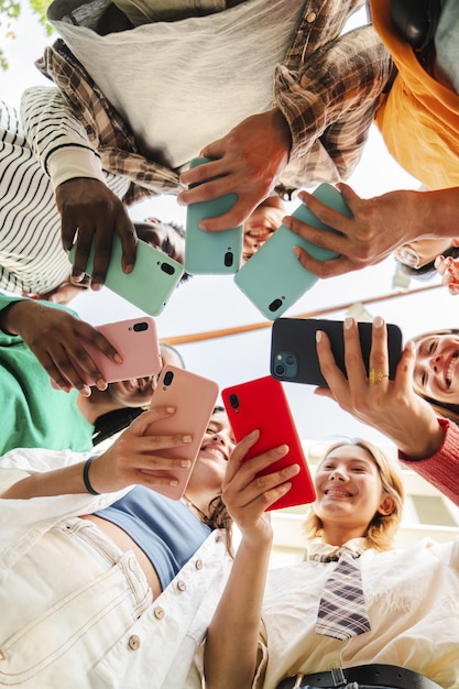 Foto vista verticale ad angolo basso di un grande gruppo di adolescenti sorridenti multirazziali dipendenti dagli smartphone