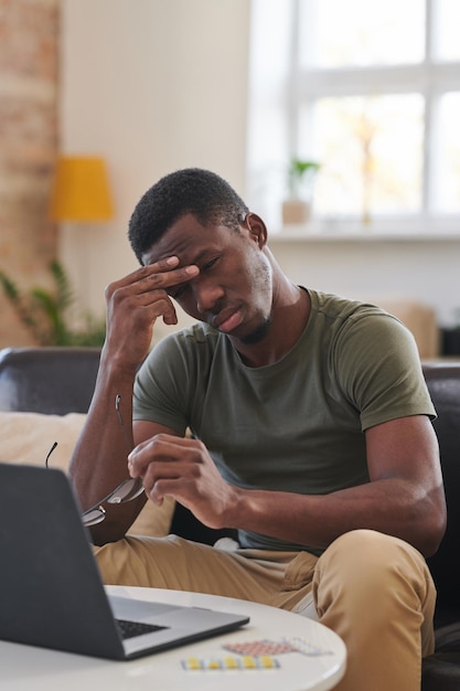 Vertical medium long shot of young adult african american man suffering headache while working on la