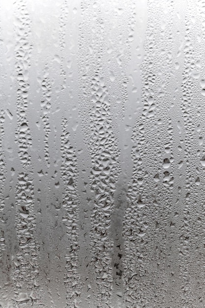 湿気と霧の空白を流れ落ちる滴を伴うガラス上の垂直の自然な背景の凝縮悪天候の雨の外