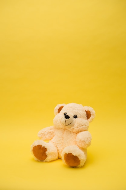 Photo vertical orientation beige bear toy on a yellow isolated background with a copy of the space