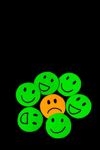 Vertical paper cutout image of green smiley faces surrounding a sad face concept of psychology therapy emotions mental health circles of trust friendship and family Black background Selective focus