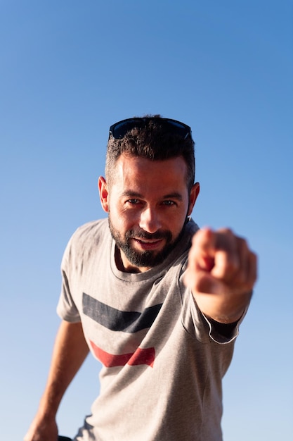 Vertical photo of a bearded man pointing finger at camera with blue sky in background copy space for text