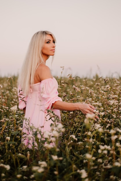 Vertical photo blonde woman posing in the big endless field of daisies in summer evening