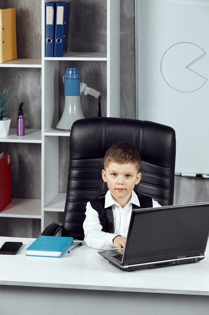 オフィスのディレクターの机に座っている男の子の縦の写真