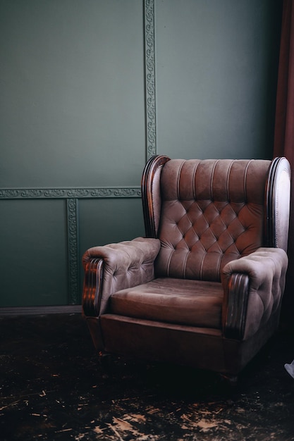 Vertical photo of a brown chair with a carriage brace A chair near the window against a green wall