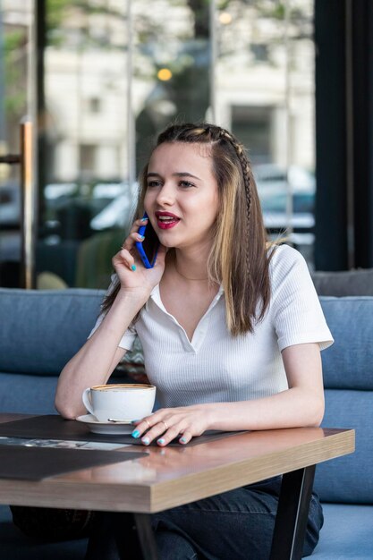 Foto verticale della signora carina seduta al ristorante e parlando al telefono