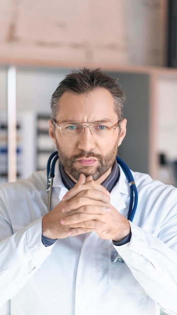 Vertical photo a doctor with a stethoscope looks closely at the camera listening to you