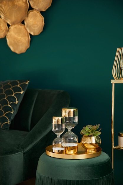 Foto foto verticale di un elegante soggiorno con pouf in velluto verde, decorazioni dorate, clessidra di design, divano e accessori eleganti. elemento di interni di lusso in una casa accogliente. modello.