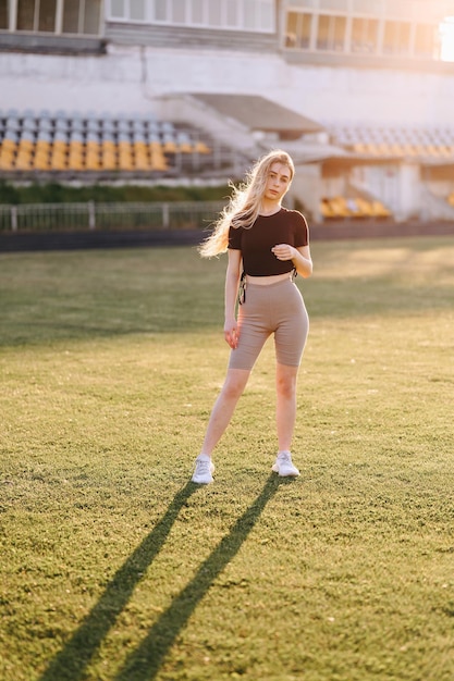 Vertical Photo Girl in Leggings and Black Top Stands Against Sun at the Stadium