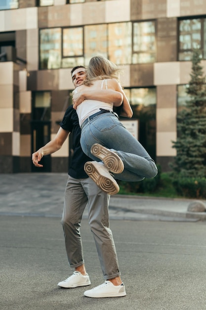 Vertical photo Happy loving couple having fun on city street guy lifted girl in arms and whirls