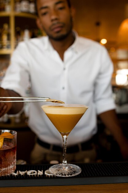 Vertical photo of latin bartender putting dried orange on top of the cocktail