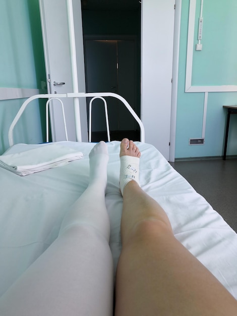 Photo vertical photo of legs in a hospital bed. right leg after a foot surgery, left legis  in compression stocking. recovery room, open door to corridor. russian hospital