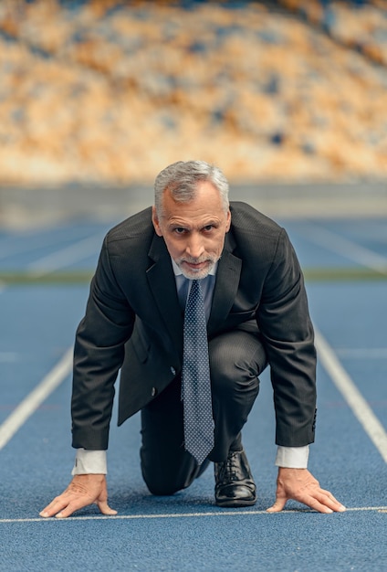 Vertical photo of man dressed in business suit and tie looking at camera while standing at start of race track preparing to run