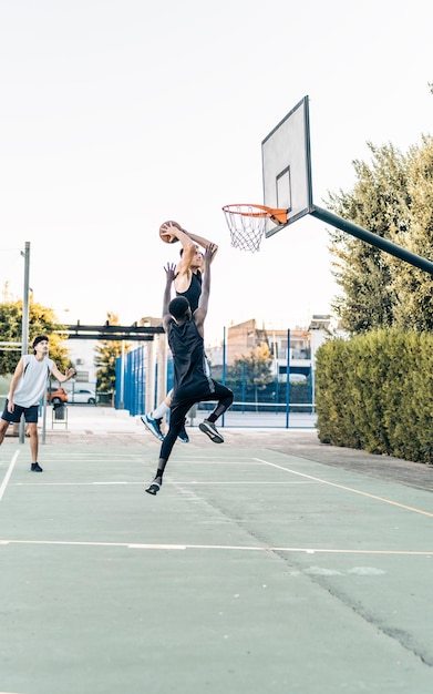 Vertical photo of a man jumping to score during a friendly basketball match between friends outdoors