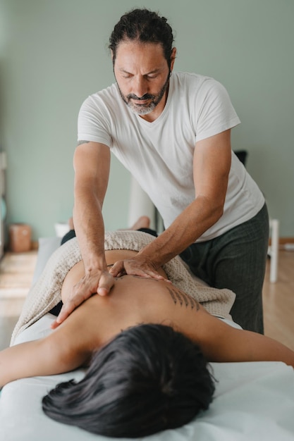 Vertical photo of a masseur giving a massage to a patient lying on a massage table