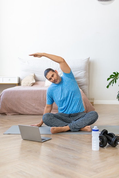 Foto verticale di un uomo di mezza età durante un allenamento di yoga a casa fumante online che si allunga indietro