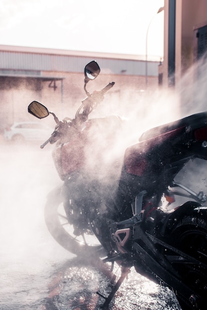 Vertical photo of pressurized water splashing on the motorcycle while washing.