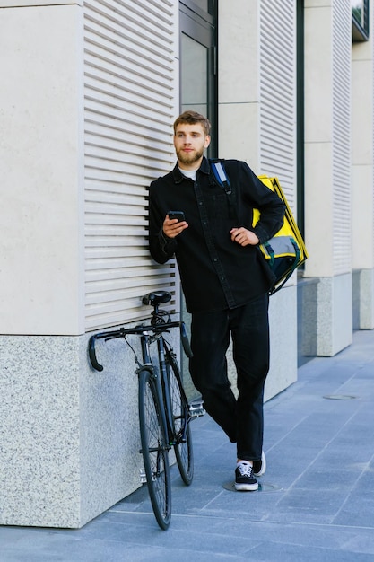 Vertical photo of a professional courier outside The courier looks at his order in the smartphone app