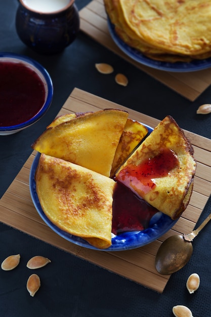 Vertical photo of pumpkin thin pancakes with berry jam on blue plate