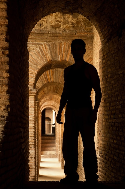 Vertical photo of a silhouette of a man in front of a wall illuminated at night. Aurelian Wall in Rome